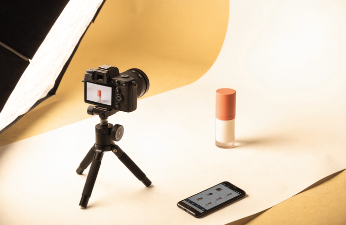 Product photography set with a camera shooting a product and an online store shown on a phone, by Clayit.